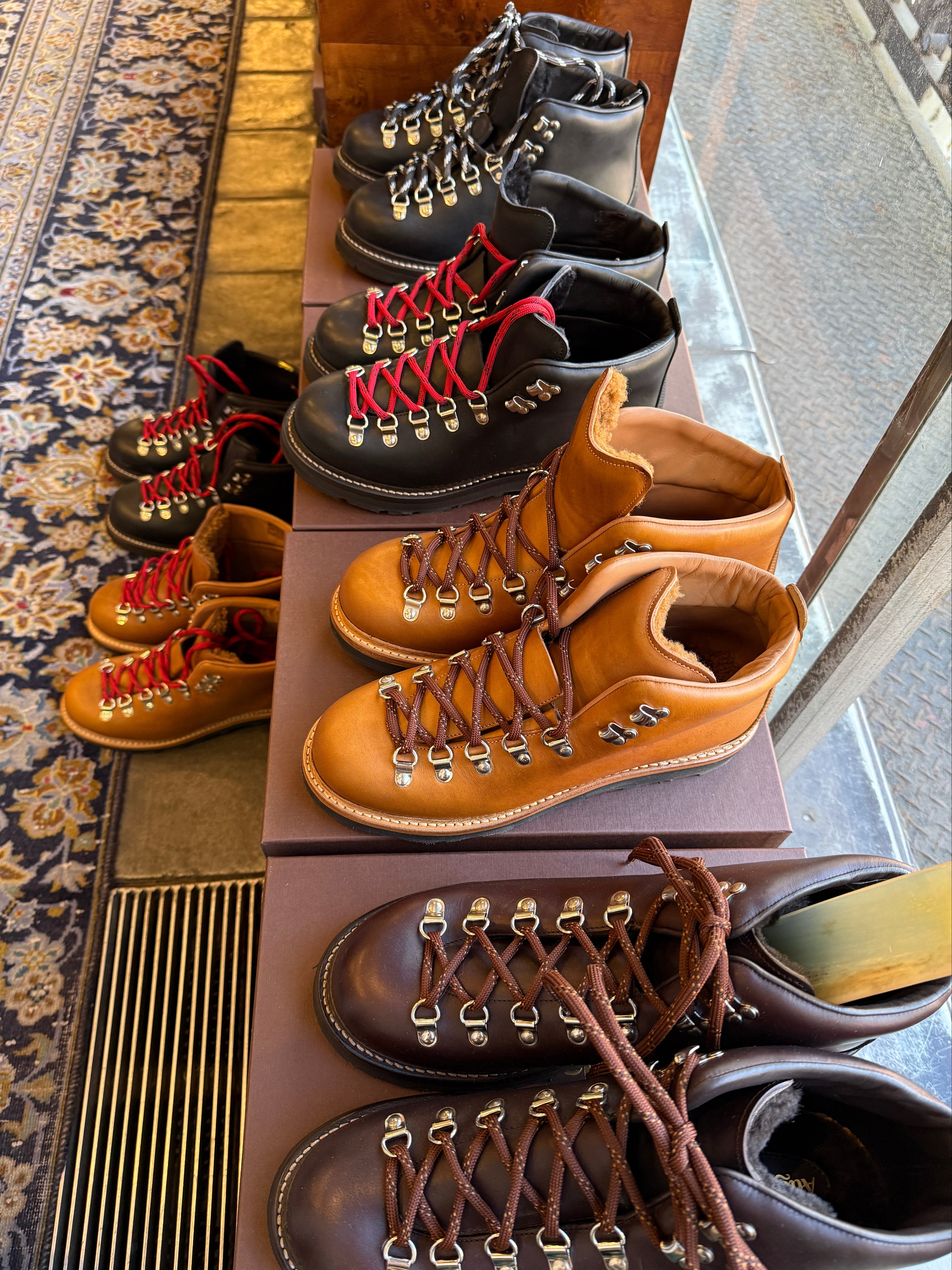 Row of leather boots displayed on a stand with a patterned floor in the background.