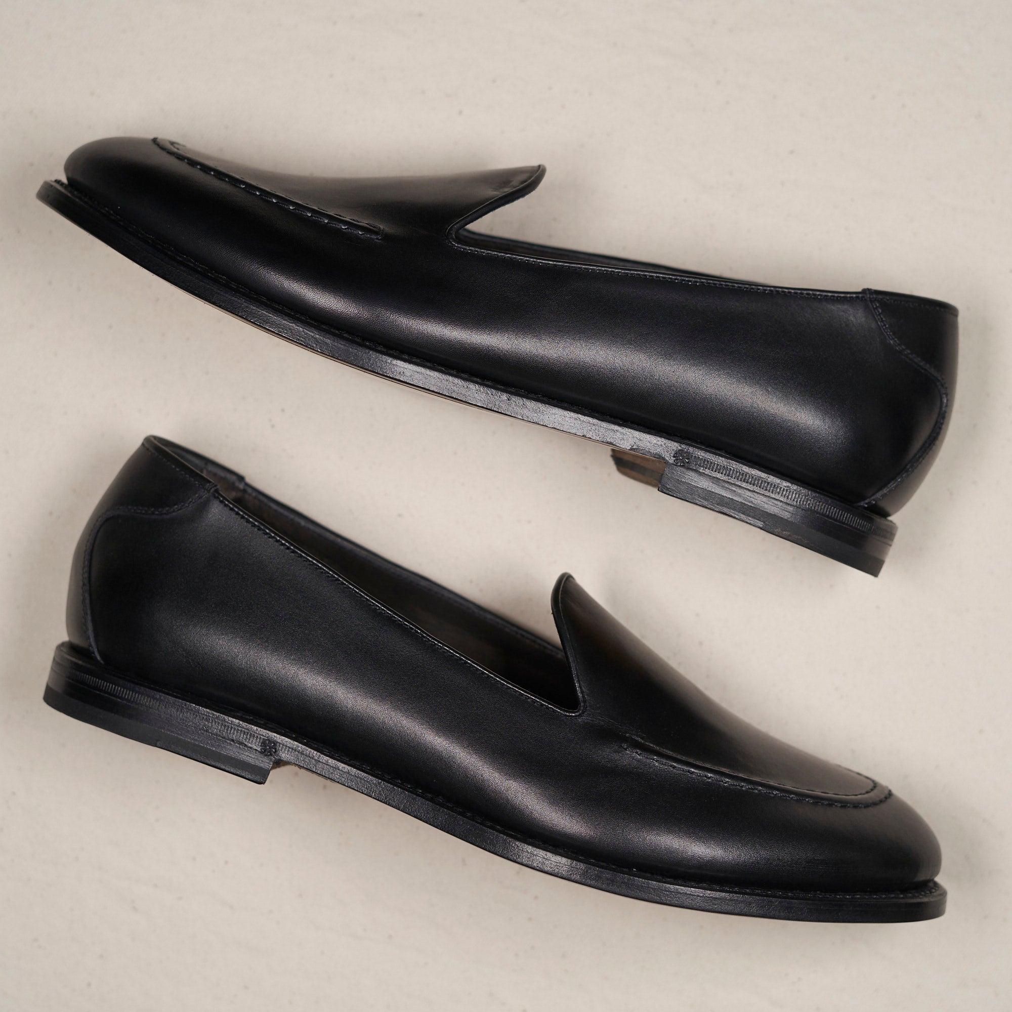 Black loafer side view against a beige backdrop