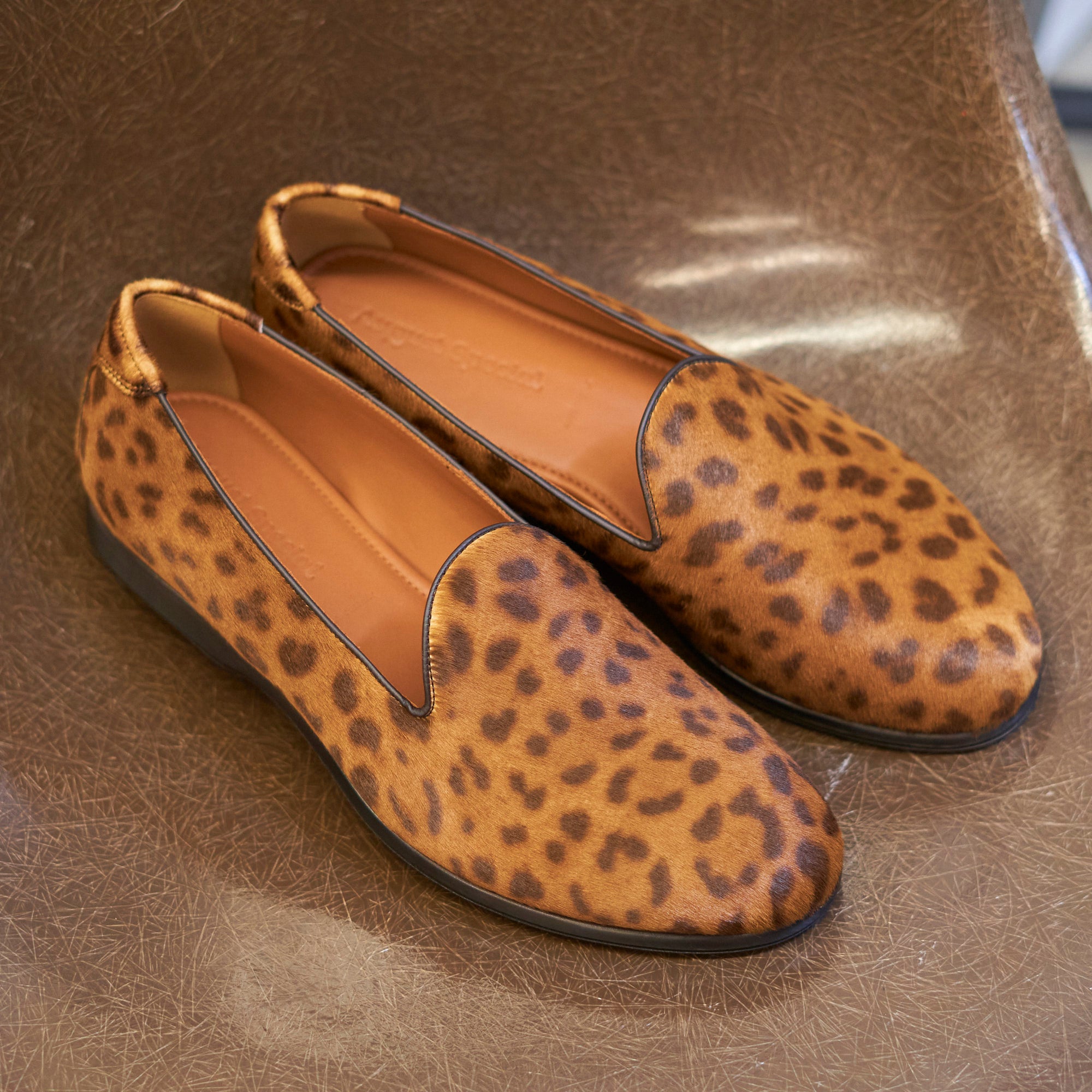 Augie Type-P Leopard Haircalf loafers – lifestyle shot, pair resting on brown leather  look surface.
