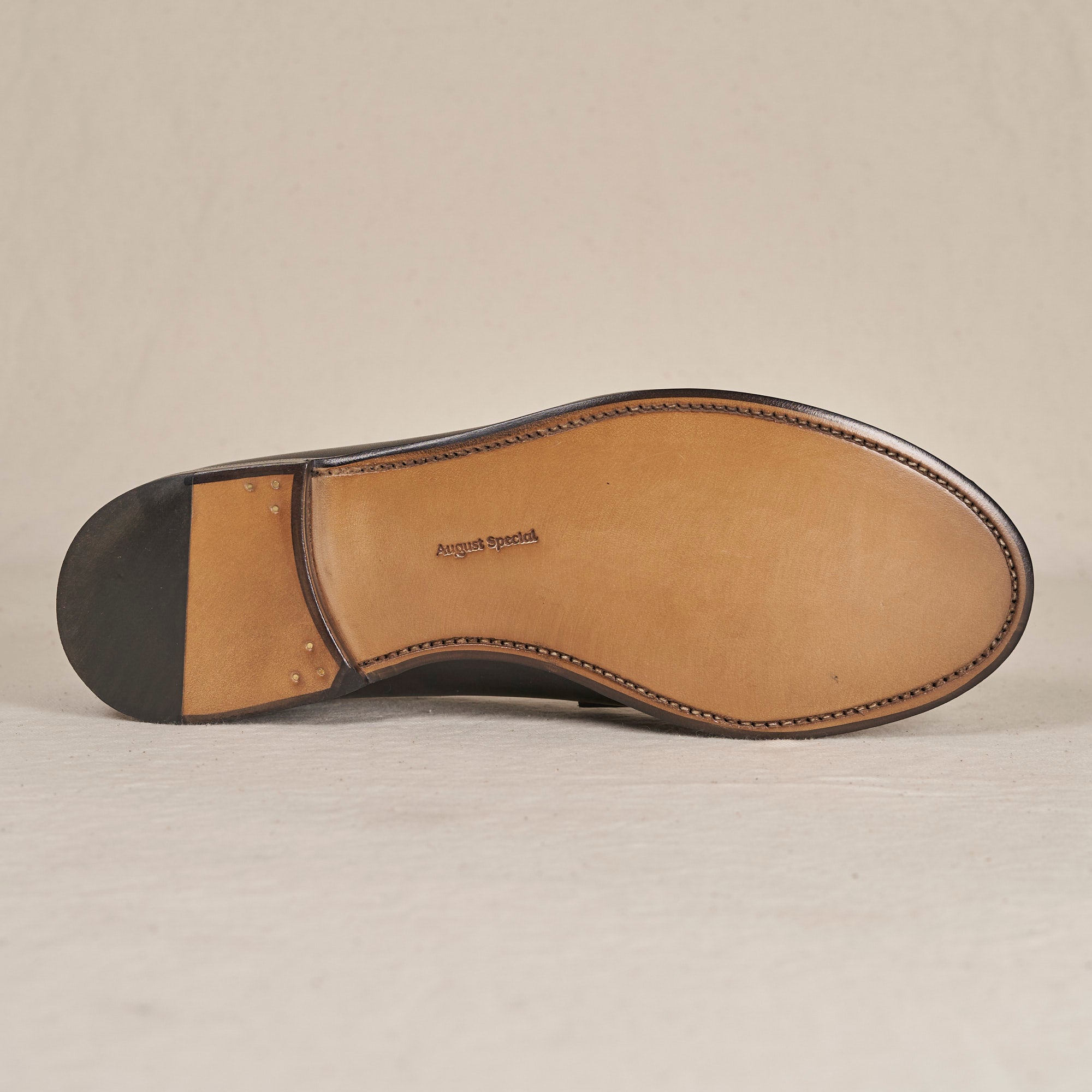 The underside of a dark brown leather dress shoe sole, showing a tan insole with 'Angus & Peterson' printed in the center, photographed against a neutral light beige background.