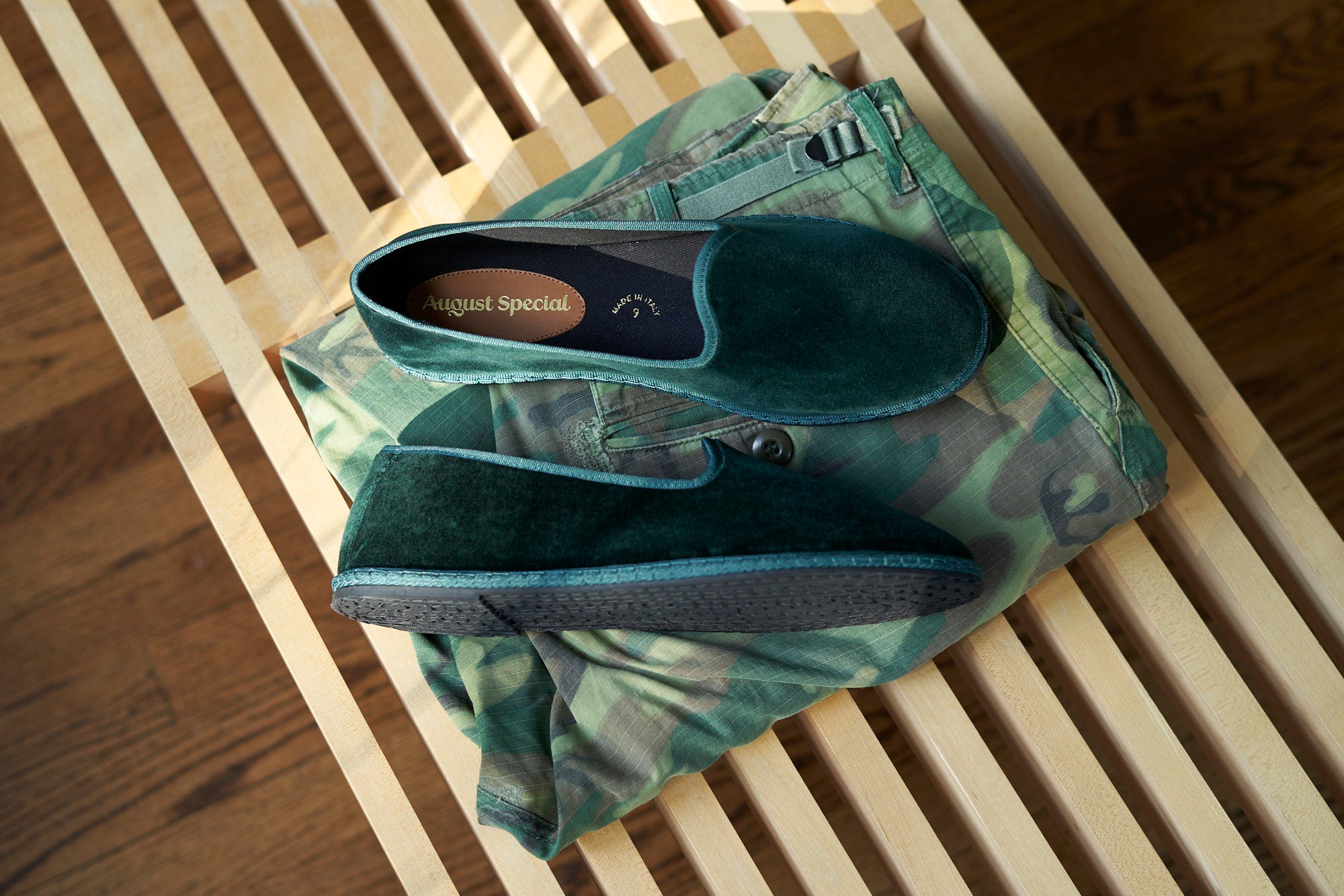 Green shoes with a brand logo on a camouflage-patterned fabric on a wooden surface