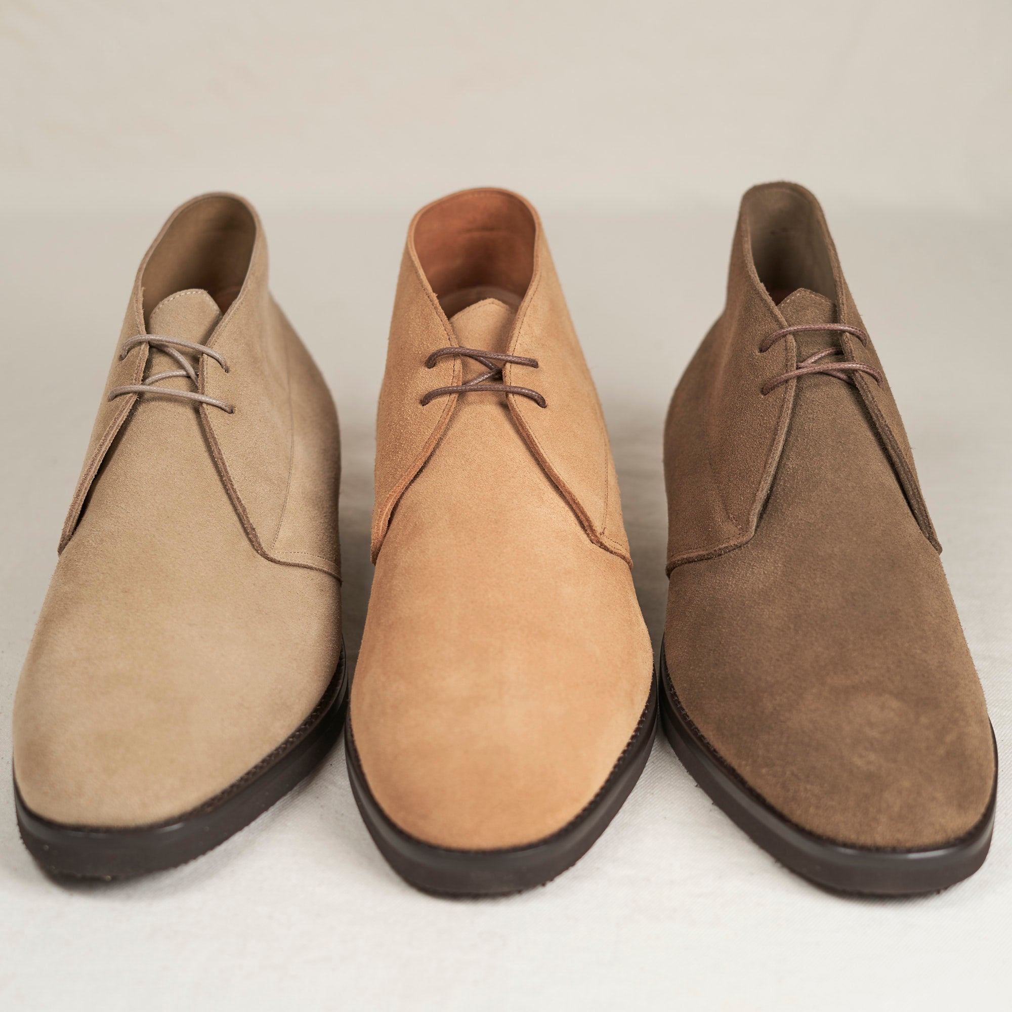 Three pairs of brown suede shoes on a light gray background