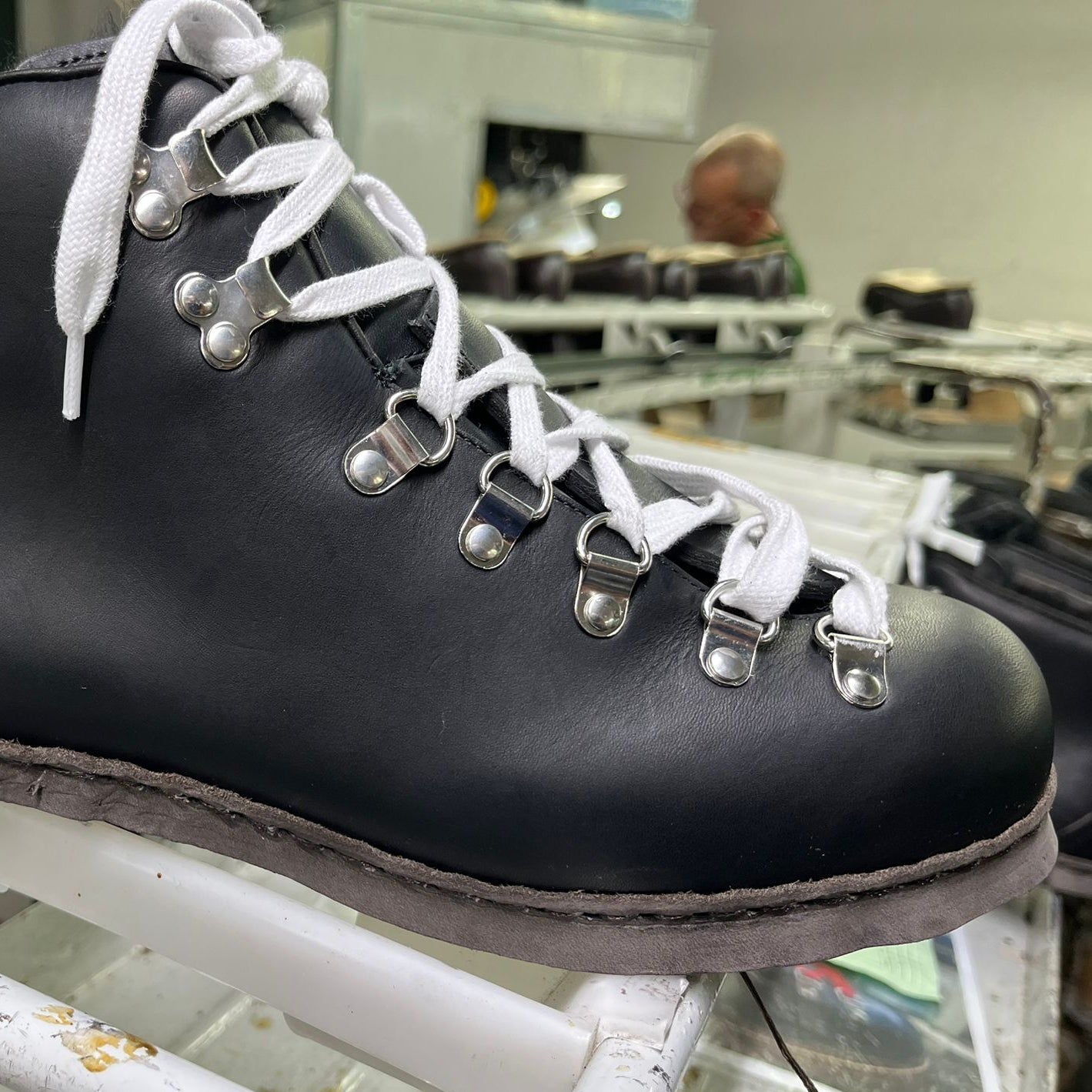 Black leather boot with white laces on a metal rack in an industrial setting.